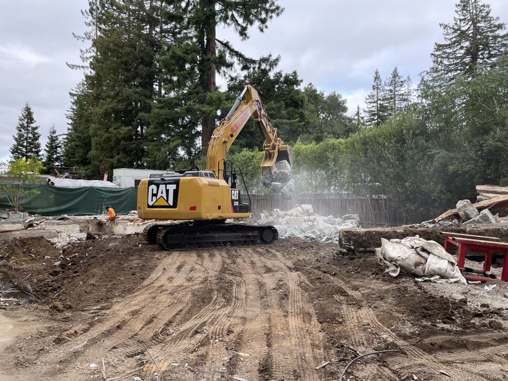 CAT excavator lifting debris during a post-disaster site cleanup, showing the essential work of demolition companies in preparing for recovery and rebuilding.